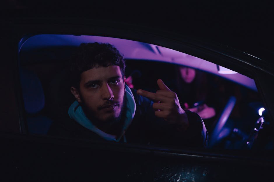 Portrait of a man in a car at night showing a middle finger gesture.