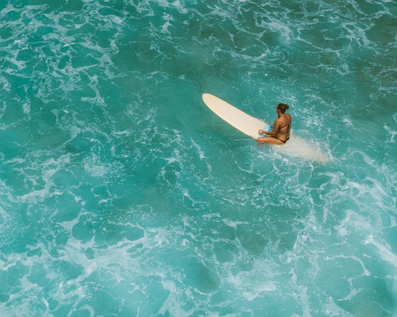 A lone surfer sits on a surfboard amidst vibrant turquoise waves in Hawaii.