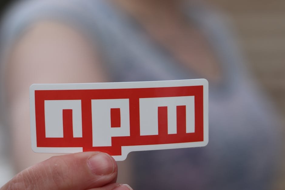 Blurred background close-up of a hand holding an npm sticker, ideal for web development themes.