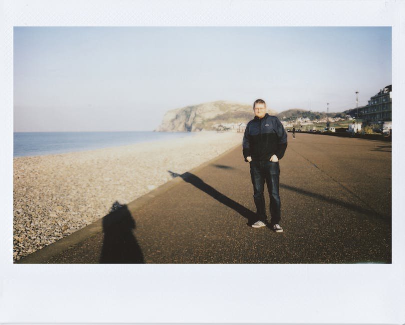 Man walking on a seashore promenade with mountains in the background.