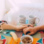 A cozy breakfast scene with two mugs, holding hands, and a colorful table setting.