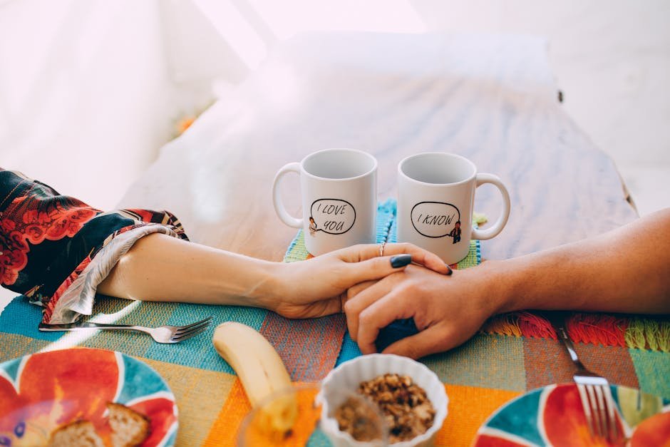 A cozy breakfast scene with two mugs, holding hands, and a colorful table setting.