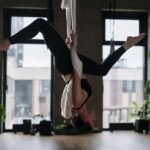 A woman performing aerial yoga in an indoor studio, emphasizing fitness and wellness.