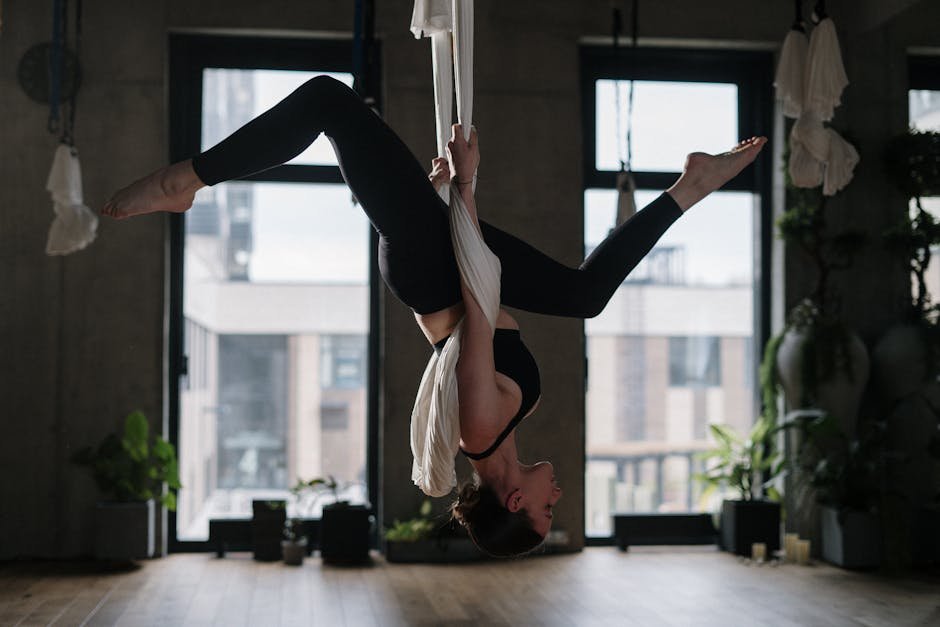 A woman performing aerial yoga in an indoor studio, emphasizing fitness and wellness.