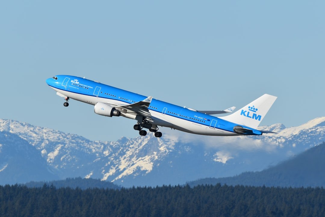 A blue and white airplane flying over a mountain range